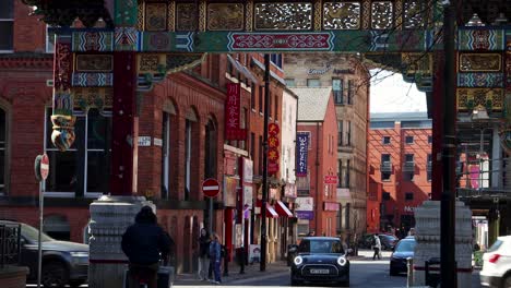 Vibrant-Chinatown-gateway-in-Manchester-with-pedestrians-and-cars-on-sunny-day,-city-life