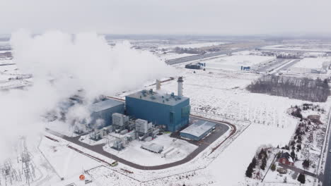 A-large-industrial-plant-emitting-steam-in-a-snowy-landscape,-winter,-aerial-view