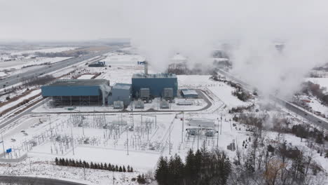 Eine-Industrieanlage-Im-Winter,-Schneebedeckte-Landschaft,-Mit-Sichtbaren-Emissionen-Und-Infrastruktur,-Luftaufnahme