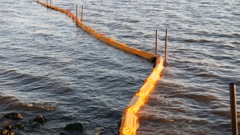 Protective-shore-barrier-floating-on-sea,-held-in-place-by-metal-rods