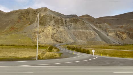 Rugged-Icelandic-landscape-with-mountains,-road-view-from-moving-car,-cloudy-day