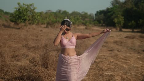 Woman-in-pink-saree-posing-gracefully-in-a-dry-field,-natural-daylight