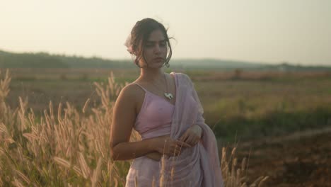 Woman-in-traditional-sari-standing-thoughtfully-in-a-golden-field-at-dusk,-gentle-breeze,-serene-expression