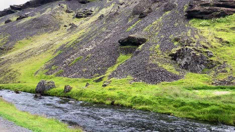 Panning-across-scenic-Kvernufoss-rushing-river-and-moss-covered-Icelandic-craggy-mountain-slopes