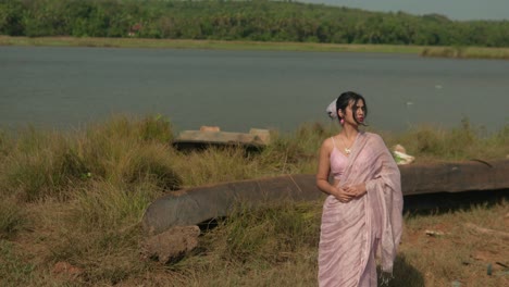 Woman-in-traditional-saree-by-riverside,-grass-and-boat,-serene-mood,-sunny-day,-static-shot