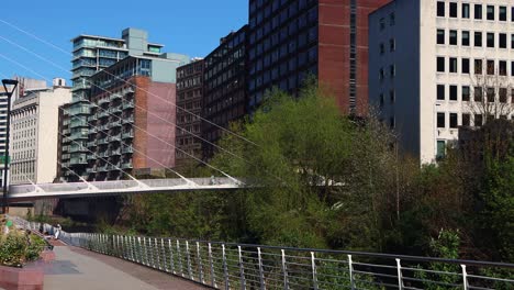 Sonniger-Tagesblick-Auf-Die-Fußgängerbrücke-In-Manchester-Mit-Stadtgebäuden-Im-Hintergrund,-Klarer-Himmel