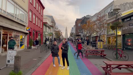 Calle-Colorida-En-Reykjavik-Con-Peatones,-Edificios-Vibrantes-Y-El-Icónico-Hallgrimskirkja-Al-Fondo
