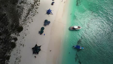 Los-roques-beach-in-venezuela-with-colorful-umbrellas-and-a-boat-on-clear-turquoise-waters,-aerial-view