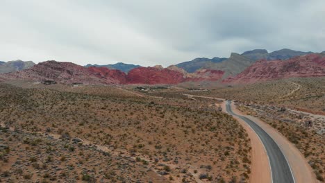 Aerial-drone-shot-of-an-empty-desert-road-with-scenic-mountains-in-the-background