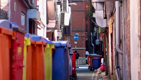 Alleyway-in-Manchester's-Chinatown-with-colorful-bins-and-walking-people,-daylight