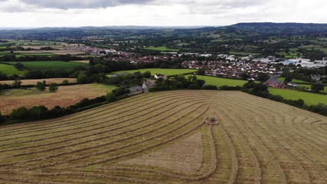 Aerial-Flying-Over-Farmland-In-East-Devon-With-Tractor-Harvesting-Hay