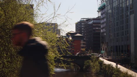 Spring-day-in-Manchester-with-bridge-over-river,-modern-buildings-in-background,-and-budding-trees-in-foreground