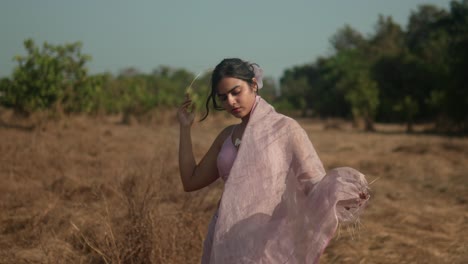 Woman-in-pink-dress-with-flowing-veil-in-dry-field,-evokes-feeling-of-freedom-and-elegance,-sunny-day