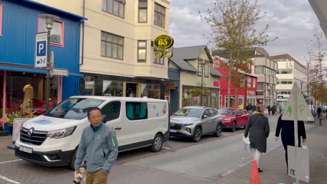 Pedestrians-and-cars-on-vibrant-Reykjavik-street,-with-colorful-buildings-and-urban-vibe,-daytime