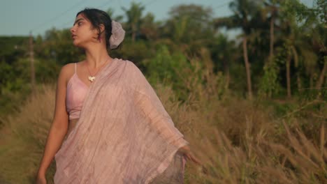 Woman-in-traditional-saree-walking-through-a-field-at-sunset,-reflective-mood