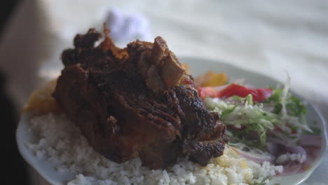 A-close-up-image-capturing-a-savoury-traditional-pork-dish-in-Cusco,-Peru,-known-as-"chicharrón-de-chancho,"-served-with-rice-and-accompanied-by-vegetables-on-the-side