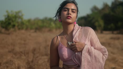 Woman-in-pink-saree-standing-contemplatively-in-rural-field,-soft-focus,-daytime