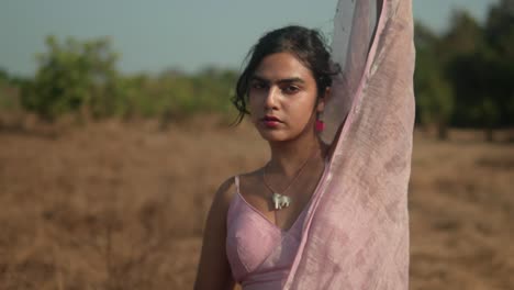 Woman-in-pink-sari-contemplating-in-a-dry-field,-warm-natural-light