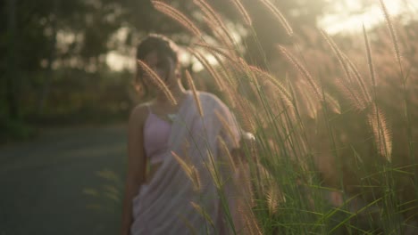 Woman-in-sari-amidst-tall-grass-at-sunset,-golden-light-filtering-through,-evoking-serenity