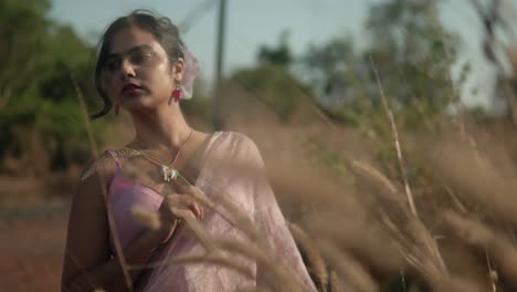 Woman-in-pink-saree-contemplating-in-a-golden-field,-shallow-focus,-warm-daylight