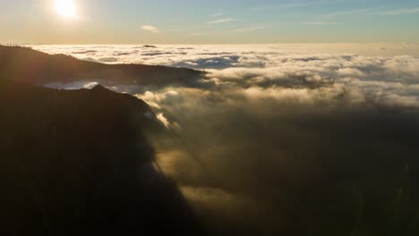 Sunrise-over-mountain-peaks-with-clouds-below,-golden-light,-aerial-view