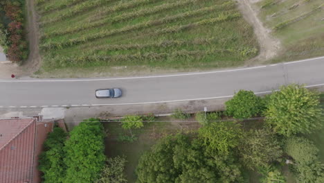 Top-down-aerial-footage-that-is-following-a-silver-car-that-is-driving-on-a-road-in-northern-Italy