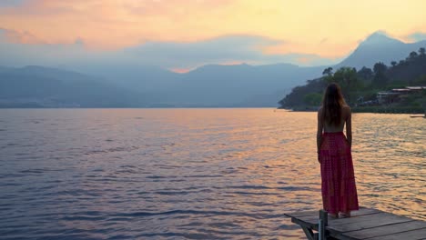 Girl-walking-on-pier-at-dramatic-sunset-at-Lake-Atitlan,-Guatemala