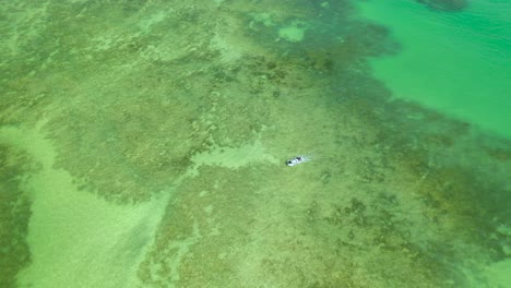 Vista-Por-Drones-De-Un-Barco-Navegando-En-Las-Piscinas-Naturales-Formadas-Entre-Arrecifes-De-Coral-En-La-Playa-De-Rua-Porto-En-Alagoas,-Brasil