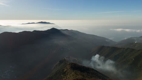 Misty-mountains-at-sunrise-in-genoa,-liguria,-with-clouds-nestled-between-peaks,-aerial-view