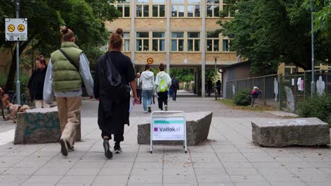 People-walking-towards-a-polling-station-in-Stockholm,-Sweden,-during-elections,-daytime,-urban-setting