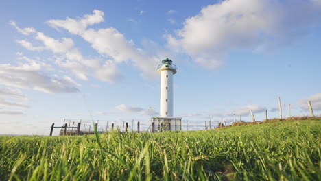 Timelapse-of-green-field-with-lighthouse-against-blue-sky-in-pure-nature-and-gently-breeze-moving-grass