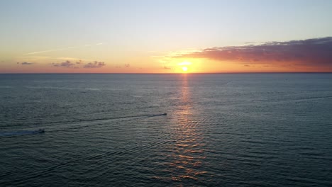 Beautiful-following-drone-shot-of-sunrise-over-the-Atlantic-Ocean-with-2-boats-in-the-distance-heading-out-to-sea