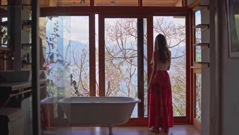 Girl-on-holiday-entering-bathroom-and-opening-window-to-lake-and-volcano-views-in-Lake-Atitlan,-Guatemala
