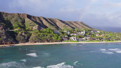 drone-footage-scanning-the-shore-of-the-island-of-Oahu-and-the-volcanic-mountain-formations-of-Diamond-Head-and-Honolulu-as-a-rainbow-forms-in-the-ocean-mist