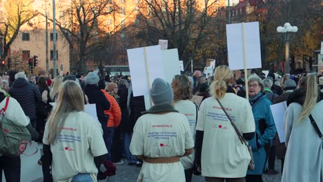 Crowd-gathered-in-Stockholm-for-a-women's-rights-protest,-placards-in-hand,-at-dusk
