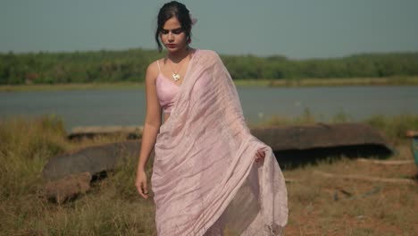 Woman-in-pink-saree-by-river-with-boat,-lush-greenery-in-background,-serene-and-cultural-mood