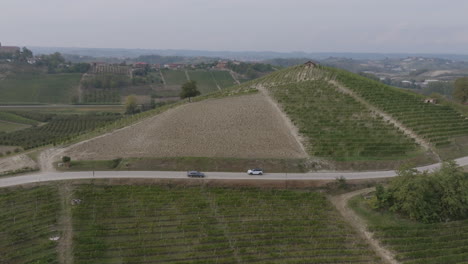 Aerial-footage-following-a-silver-sedan-as-it-drives-on-a-small-road-through-the-vineyards-and-hills-of-northern-Italy