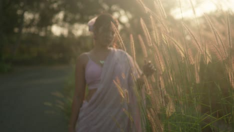 Woman-in-a-pink-dress-enjoying-the-golden-hour-amidst-tall-grass,-soft-focus,-backlit-by-the-sun