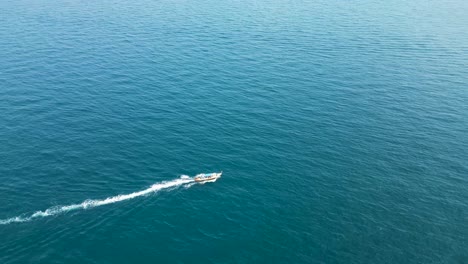 Long-tail-boat-reaching-Mango-Bay-Ko-Tao-Island-Thailand-shore-with-rocky-peninsula,-Aerial-pan-right-shot