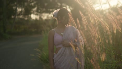 Woman-in-pink-dress-enjoying-golden-hour-in-a-grassy-field,-backlit-by-the-sun,-serene-ambiance
