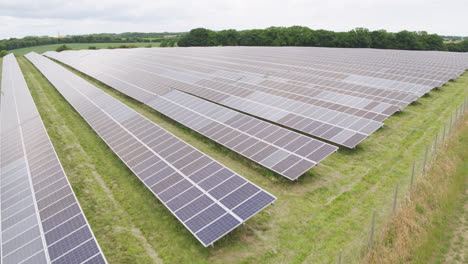 Solar-panel-farm,-aerial-footage-of-large-acre-field-covered-in-photovoltaic-panels-to-the-backdrop-of-a-english-countryside