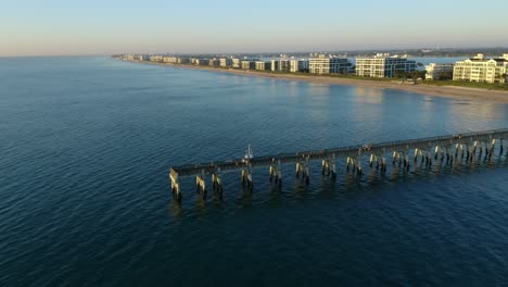 Drone-shot-heading-southwest-over-the-pier-at-Lake-Worth-Florida-toward-the-beach-and-waterfront-homes-and-condos