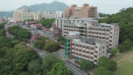 Urban-landscape-in-Taiwan,-showing-a-mix-of-residential-buildings,-trees,-and-mountains-in-the-background,-aerial-view