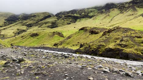 Seljavallalaug-river-flowing-under-moss-covered-misty-Icelandic-mountain-summit
