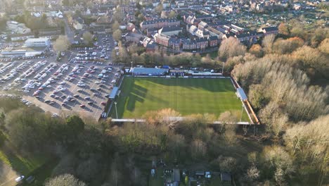 A-football-stadium-in-bury-st-edmunds,-england-with-surrounding-parking-and-trees,-daylight,-aerial-view