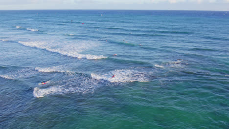 drone-footage-across-the-blue-green-waters-of-the-coast-of-Oahu-Hawaii-as-the-white-capped-waves-pound-the-surfers-and-kite-boarders-on-their-way-out-to-catch-a-wave
