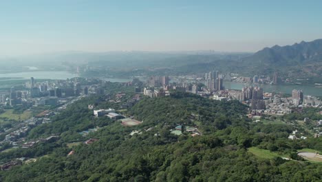 Beitou-district-with-tamsui-river,-lush-greenery,-and-urban-skyline,-Taipei,-Aerial