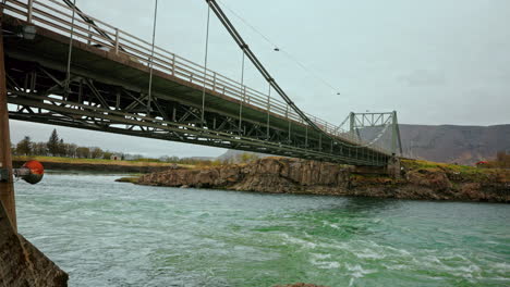 Wide-shot-of-a-metal-bridge-and-a-river-streaming-below-it-in-Iceland