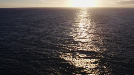 drone-footage-circling-a-kite-surfer-at-a-distance-on-the-Pacific-ocean-Honolulu-Hawaii-as-the-sun-reflects-across-the-calm-ocean-waves-as-it-prepares-to-set