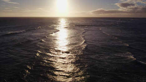 aerial-footage-of-the-golden-refection-of-the-sun-setting-on-the-Pacific-ocean-as-the-waves-travel-horizontally-to-the-shore